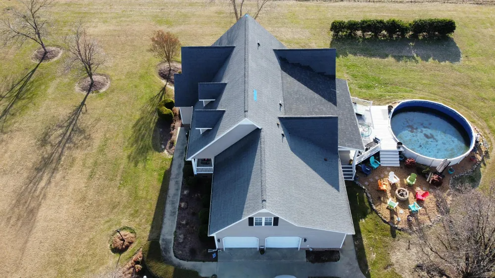 Aerial view of a house with a gray roof, backyard pool, and patio furniture.
