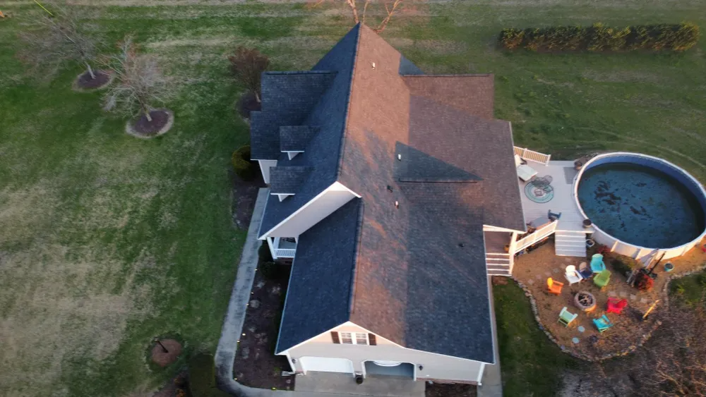 Aerial view of a house with a brown roof, grassy yard, and a round above-ground pool.