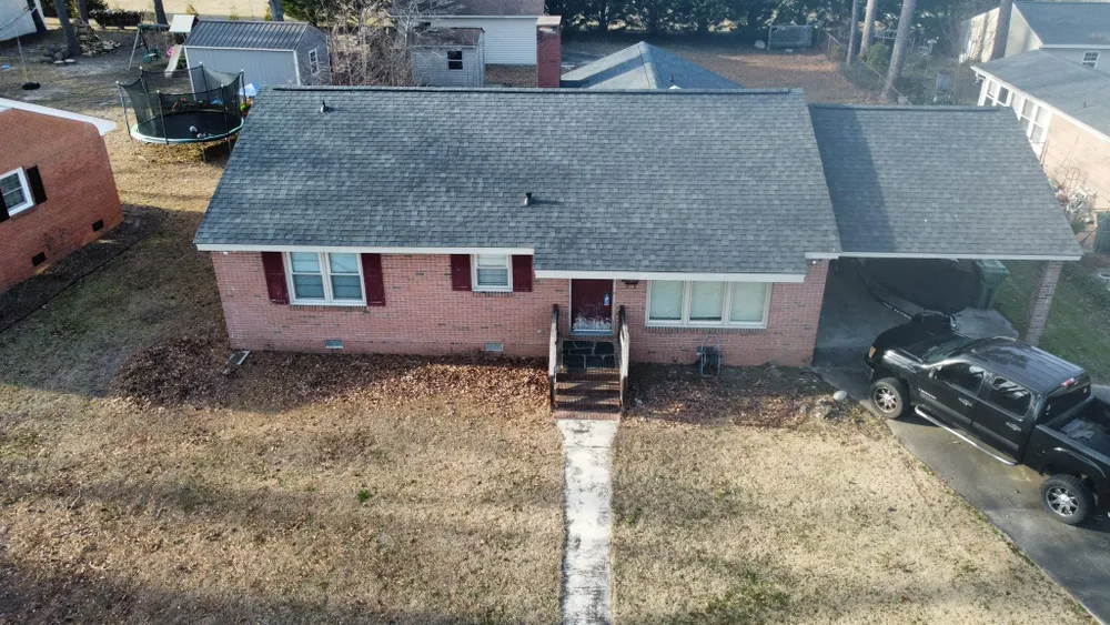 Aerial view of a red brick house with gray roof, front steps, and a parked black truck in the driveway.