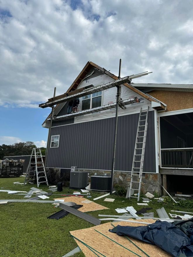 Roofing crew restoring a storm-damaged home exterior with new siding and roofline repairs