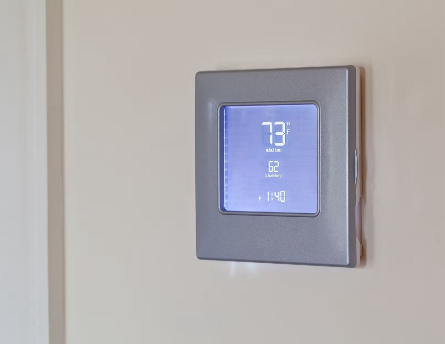 Thermostat displaying 73 degrees Fahrenheit on a beige wall, with clock and humidity displayed.