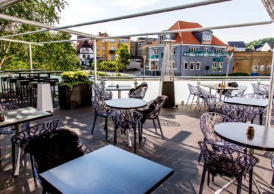 Outdoor restaurant patio with tables and chairs, overlooking a town with buildings.