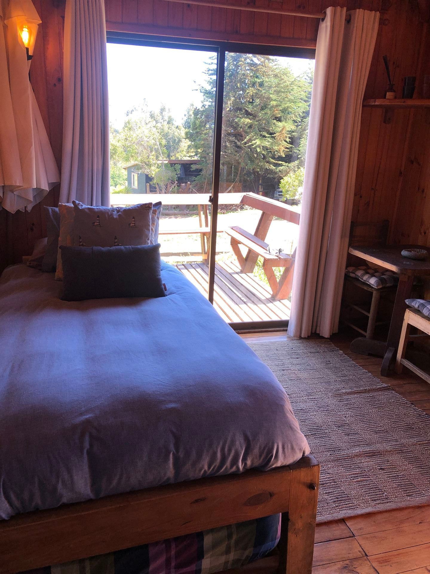 Acogedor dormitorio tipo cabaña con cama, almohadas, alfombra y puerta corrediza de vidrio que conduce a una terraza 