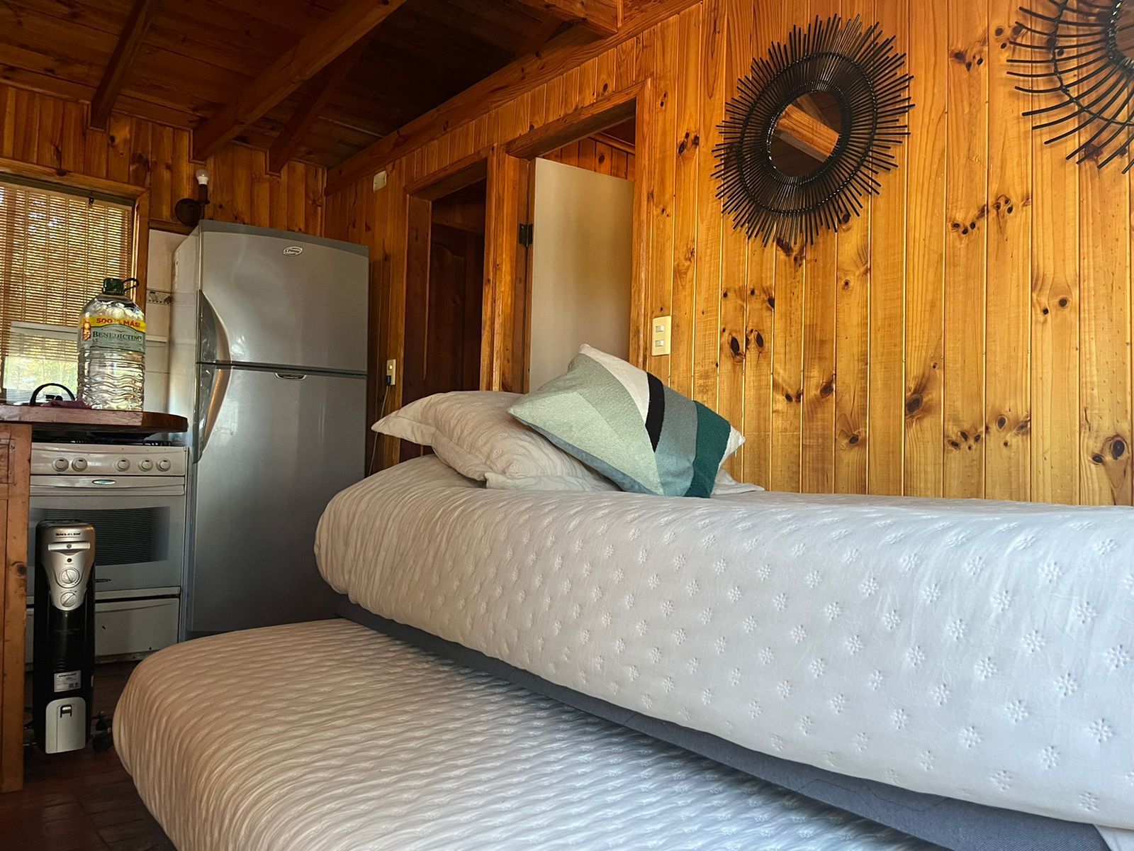 Acogedor interior de cabaña con cama, refrigerador y paredes revestidas de madera.