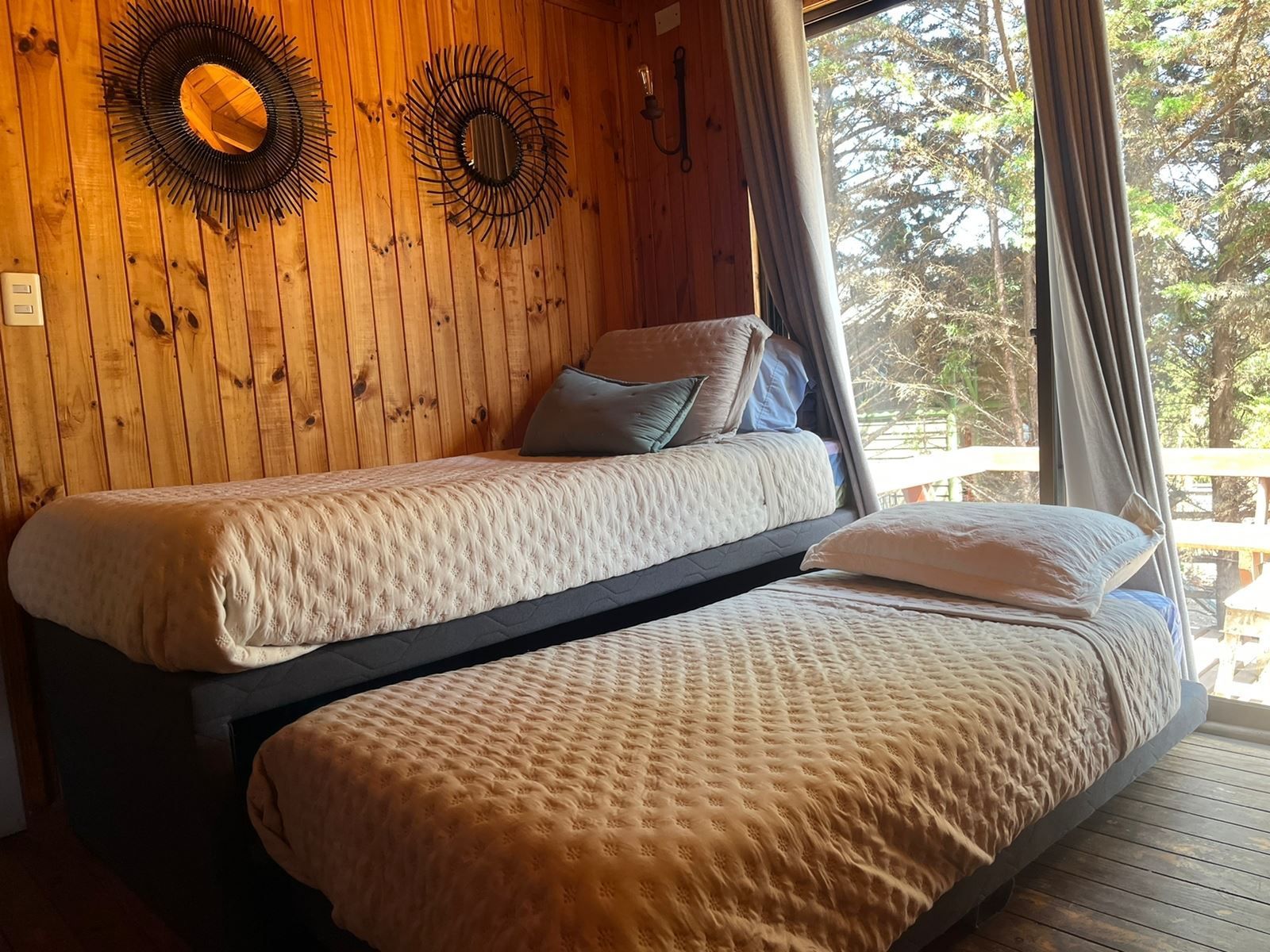 Dos camas individuales en una habitación con paneles de madera y una gran ventana con cortinas.