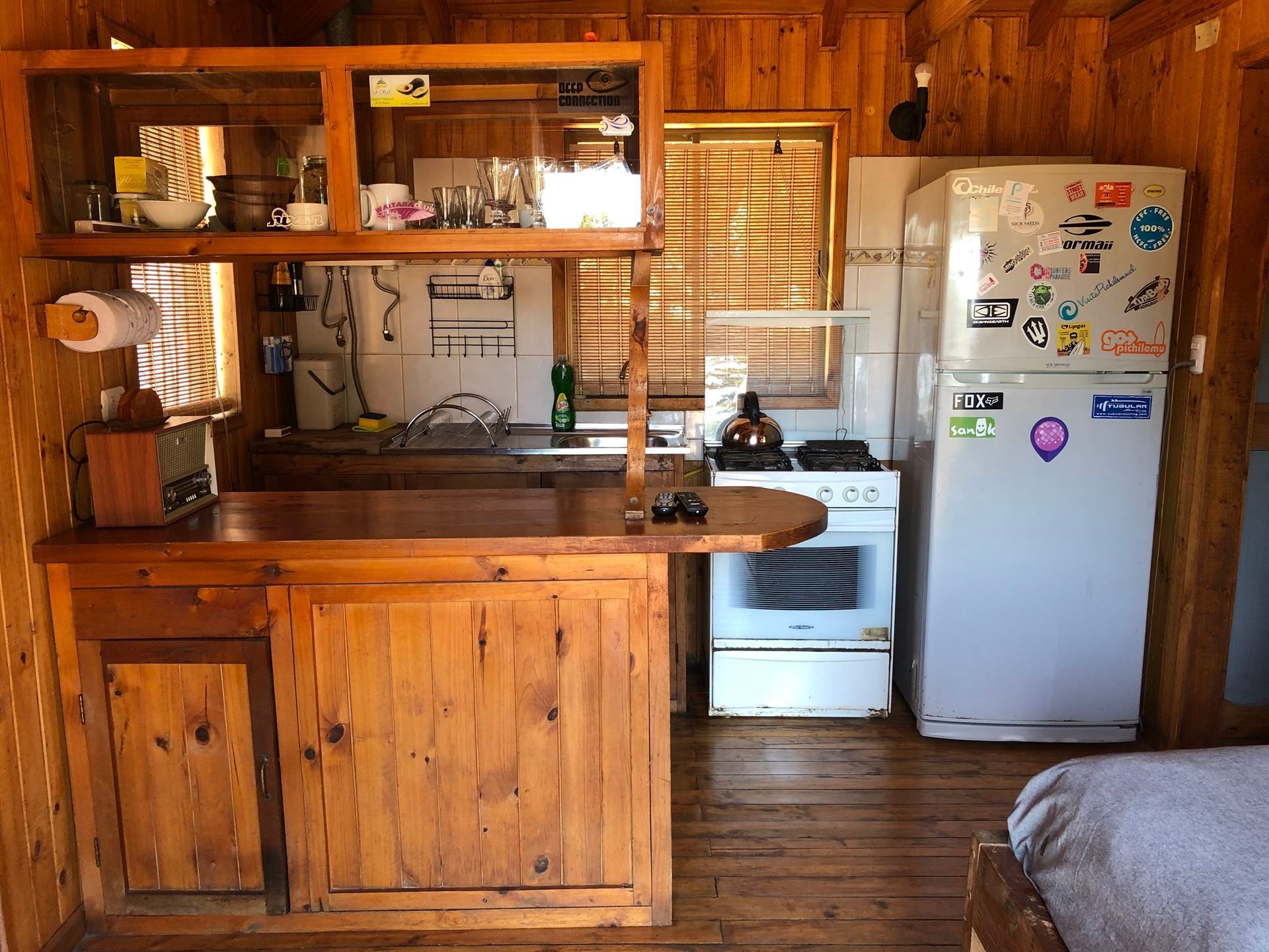 Cocina tipo cabaña de madera con encimera, electrodomésticos y ventana con persianas.