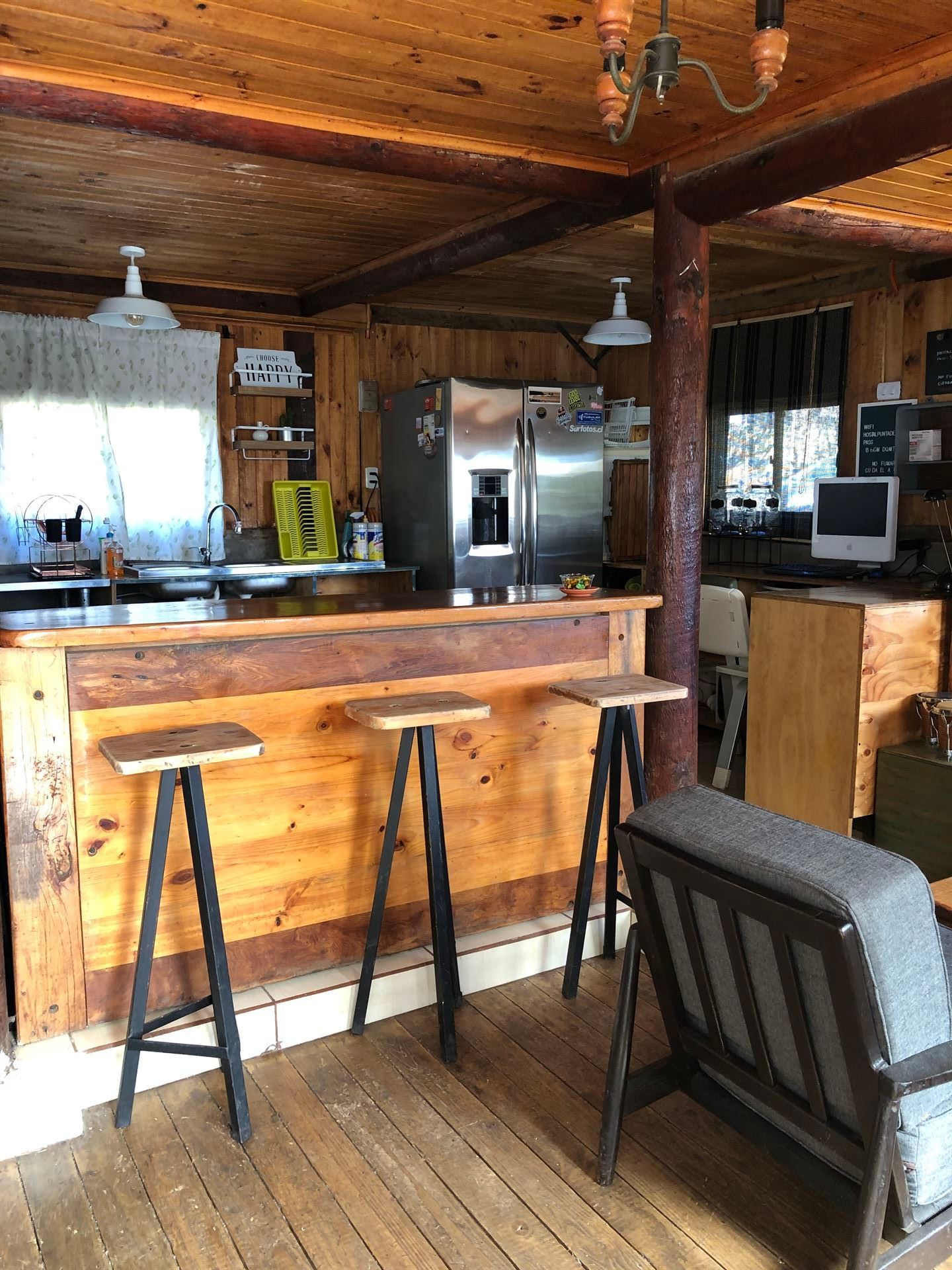 Cocina rústica con barra de madera, taburetes, refrigerador y zona de estar.