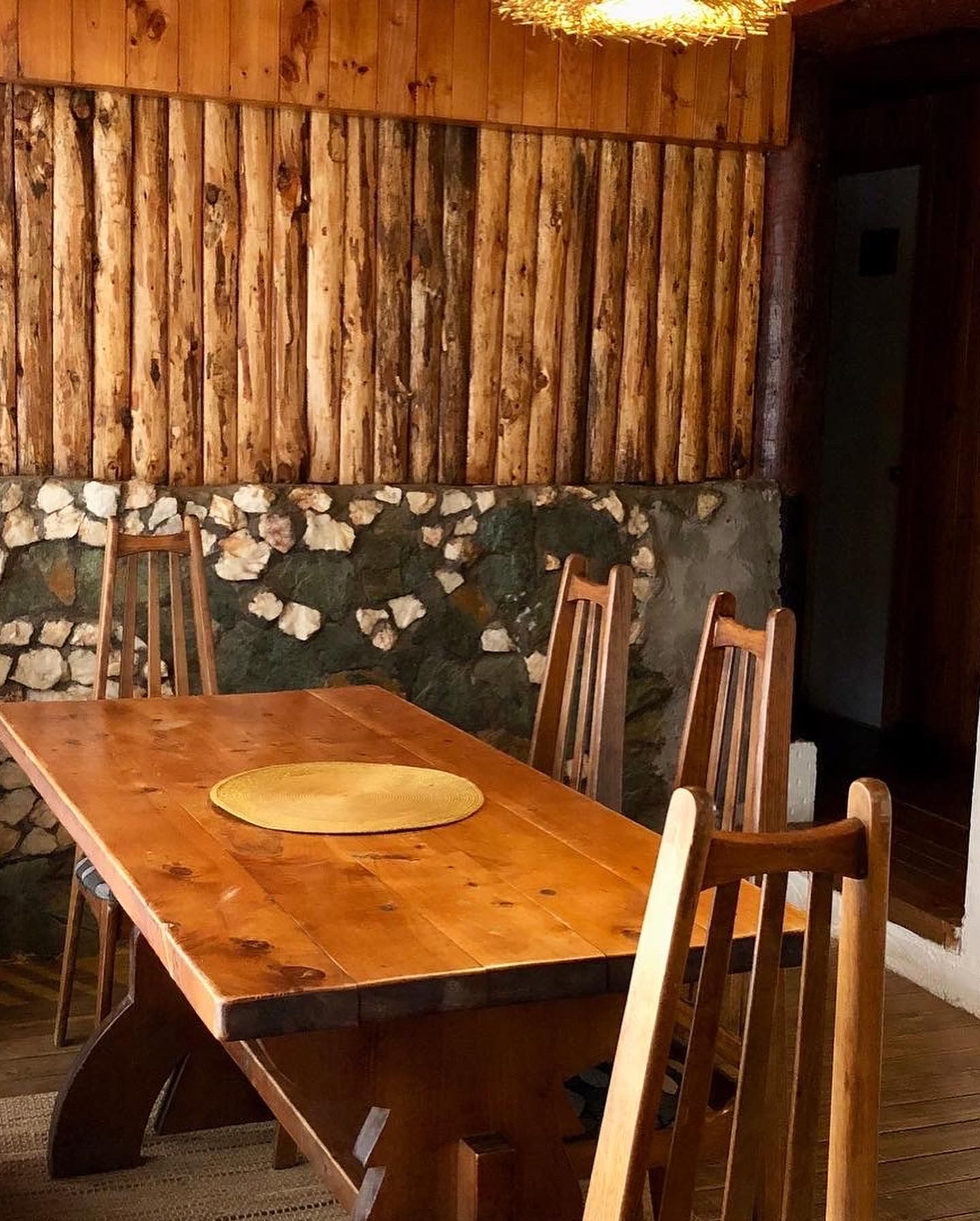 Mesa de comedor y sillas de madera en comedor rústico con paredes de troncos y piedra.