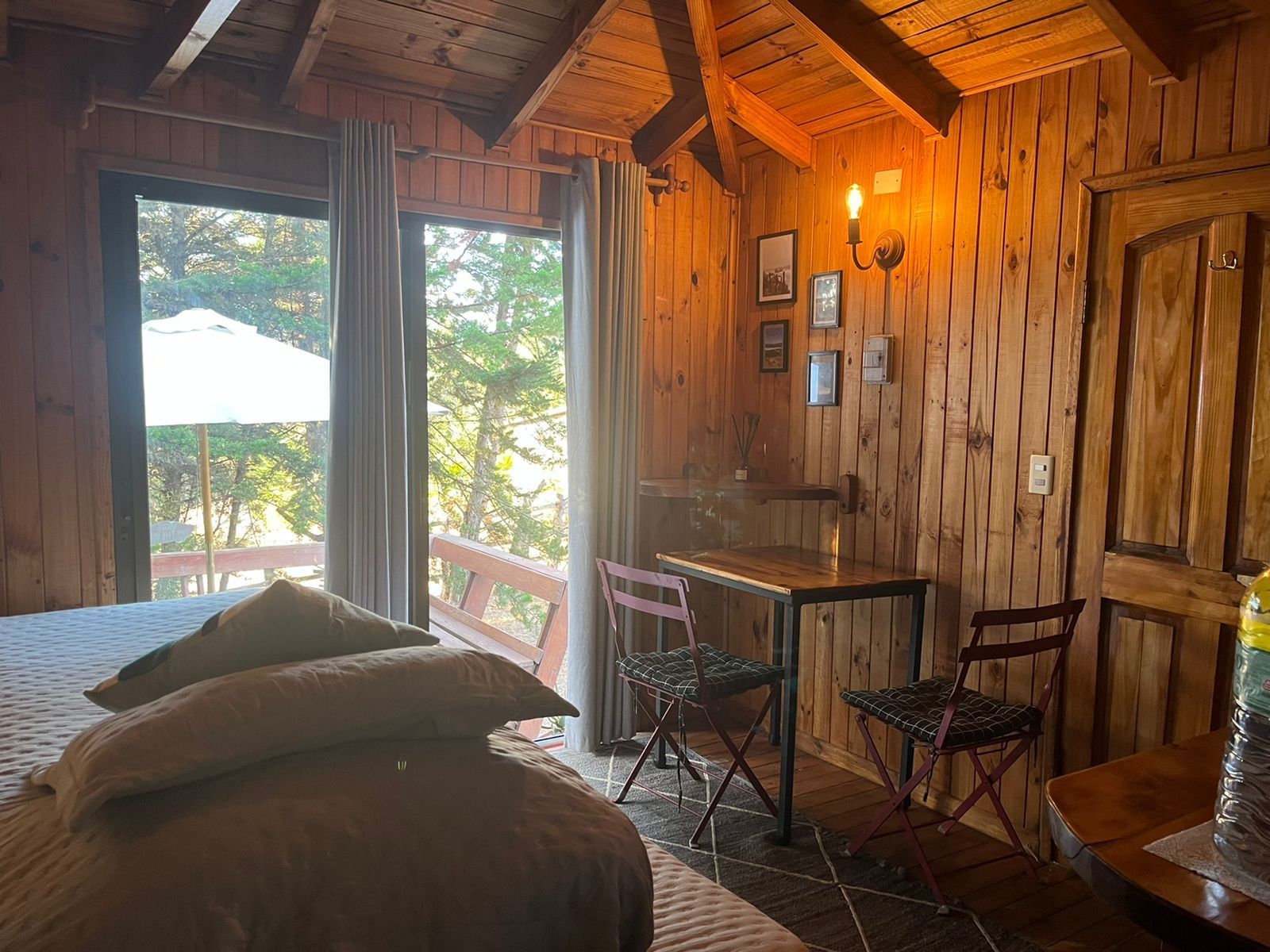 Acogedora habitación en una cabaña de madera con cama, escritorio, sillas y balcón con vistas. Luz suave y tonos cálidos.