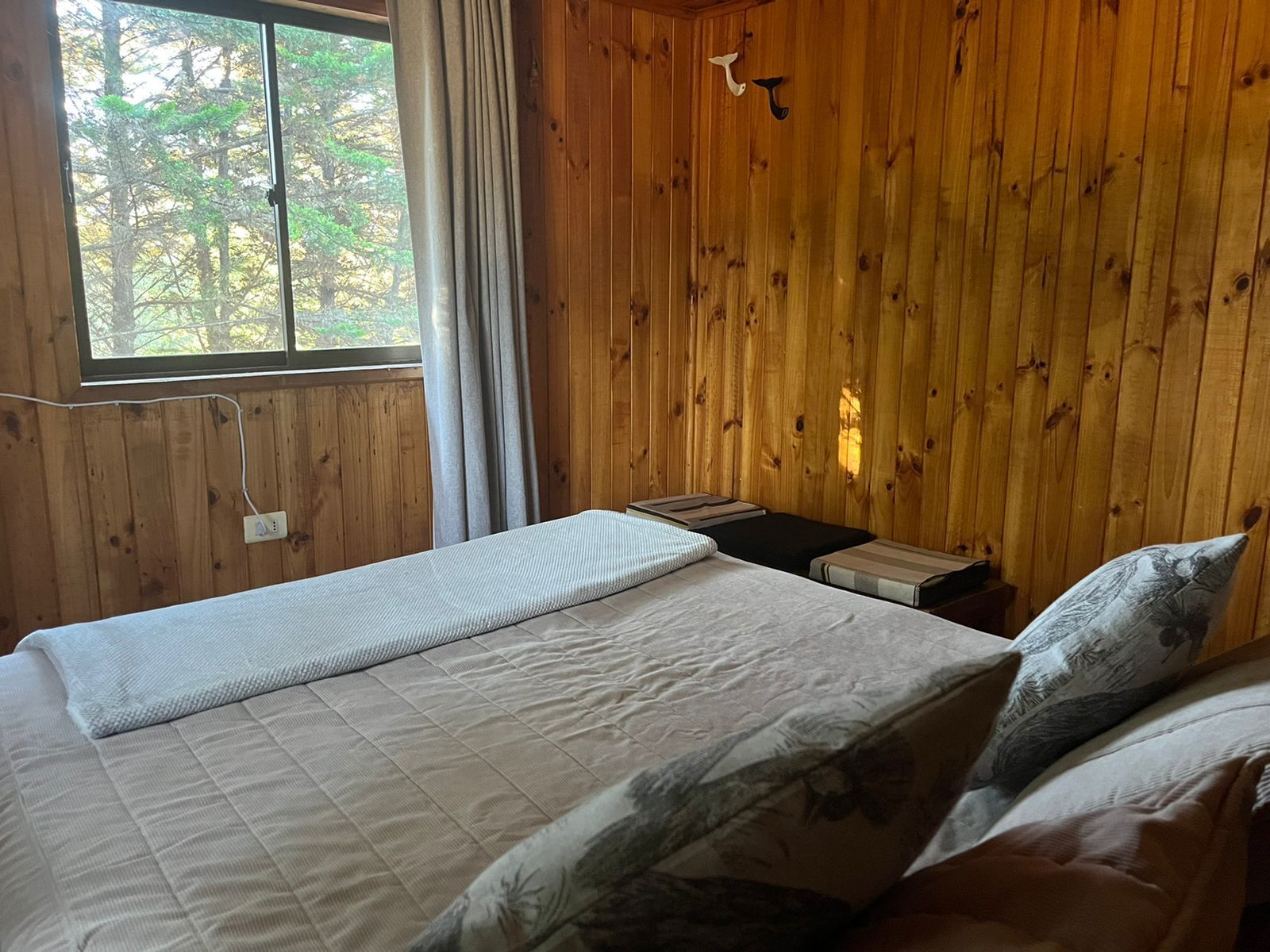 Dormitorio con paredes de madera, una cama con almohadas y una ventana con cortinas.