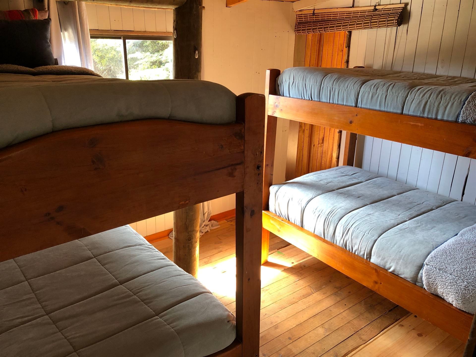 Dormitorio con dos literas de madera y una cama doble. La luz del sol entra a raudales por una ventana.