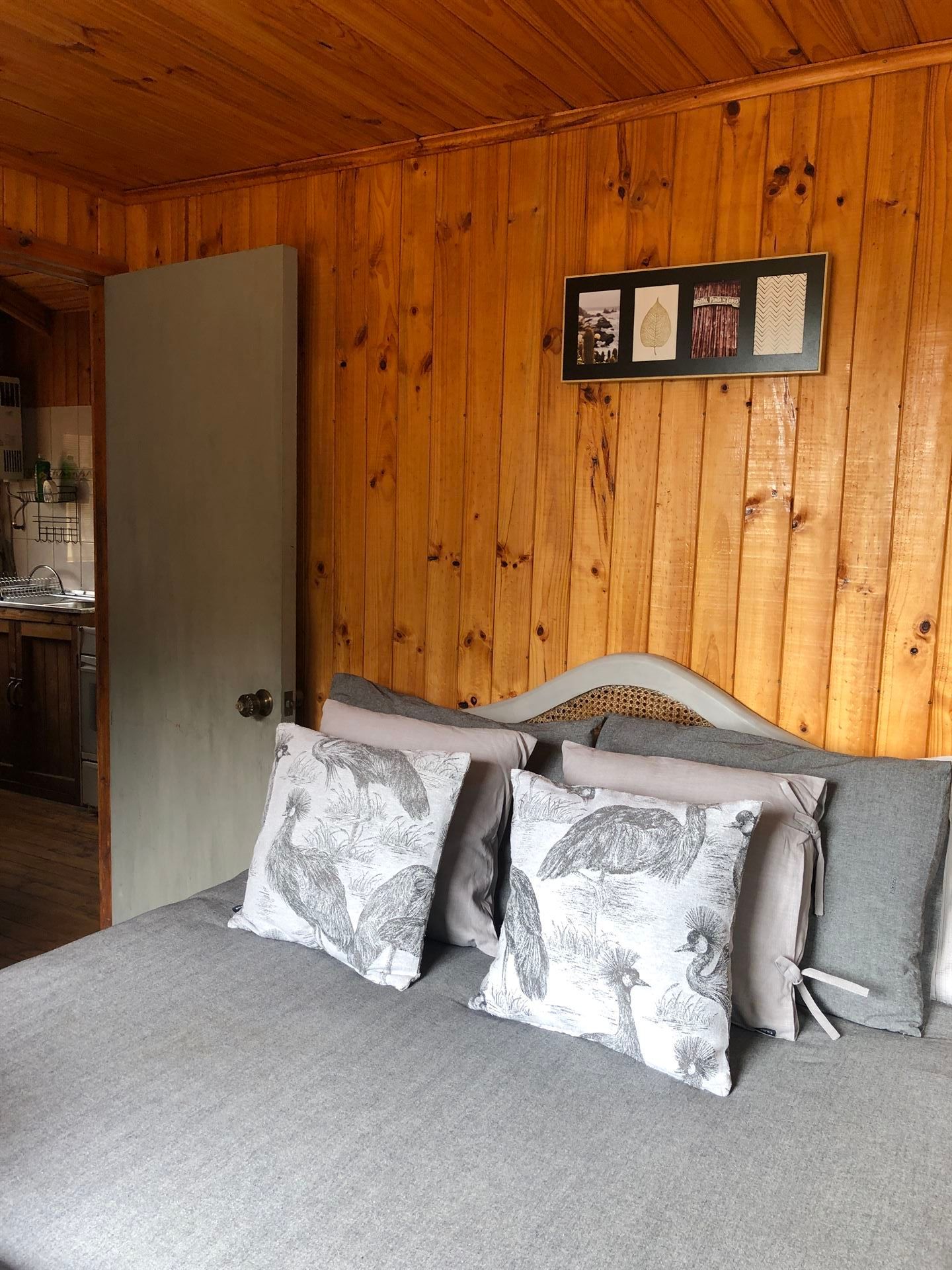 Dormitorio con paredes revestidas de madera, ropa de cama gris, almohadas estampadas y una foto enmarcada encima de la cama.