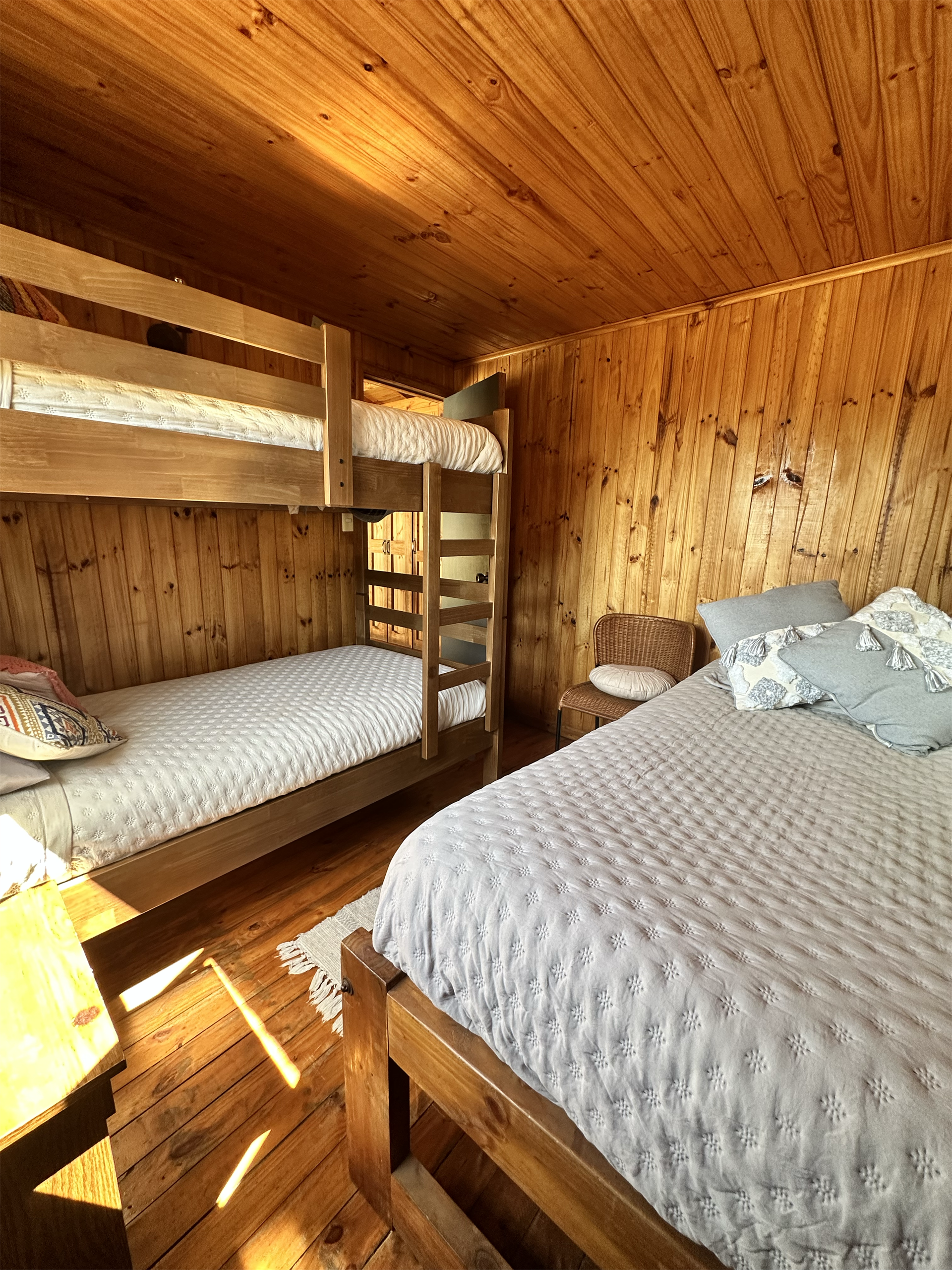 Dormitorio con paredes y techo de madera; litera y una cama doble.