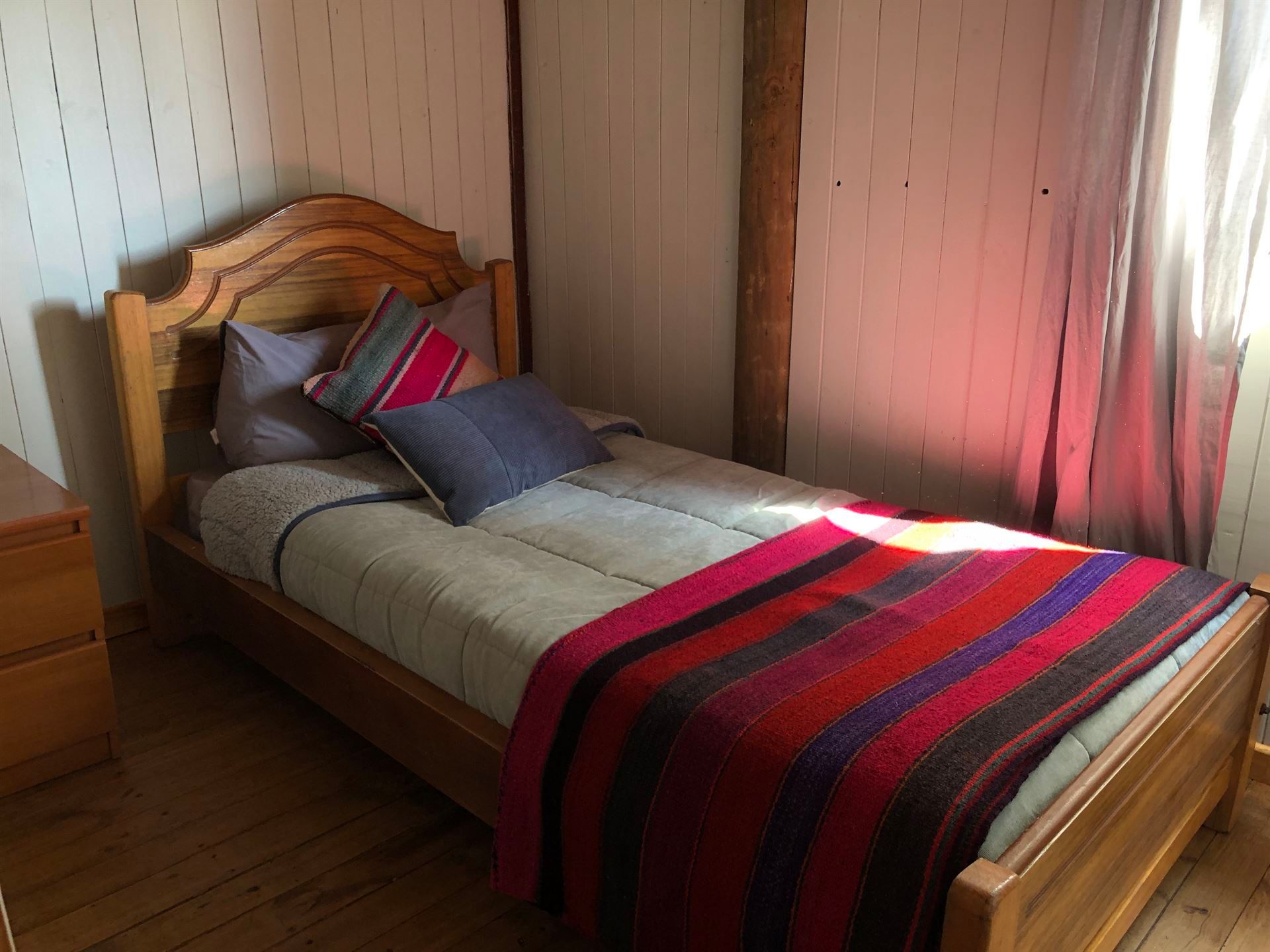 Dormitorio con cama de madera, paredes blancas y manta y almohadas de rayas de colores.