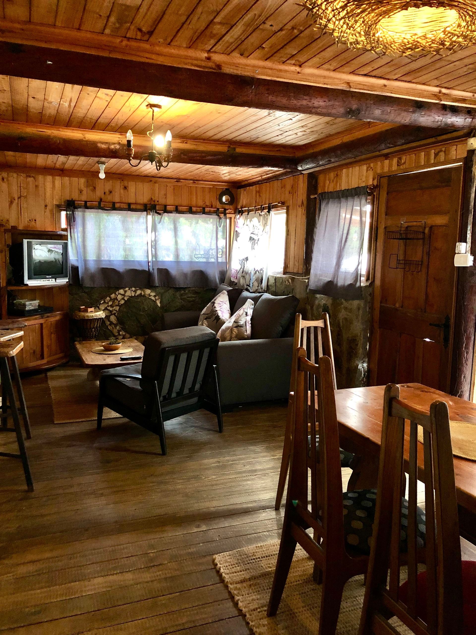 Acogedor interior de cabaña con paneles de madera, zona de estar con sofá y sillones y mesa de comedor.