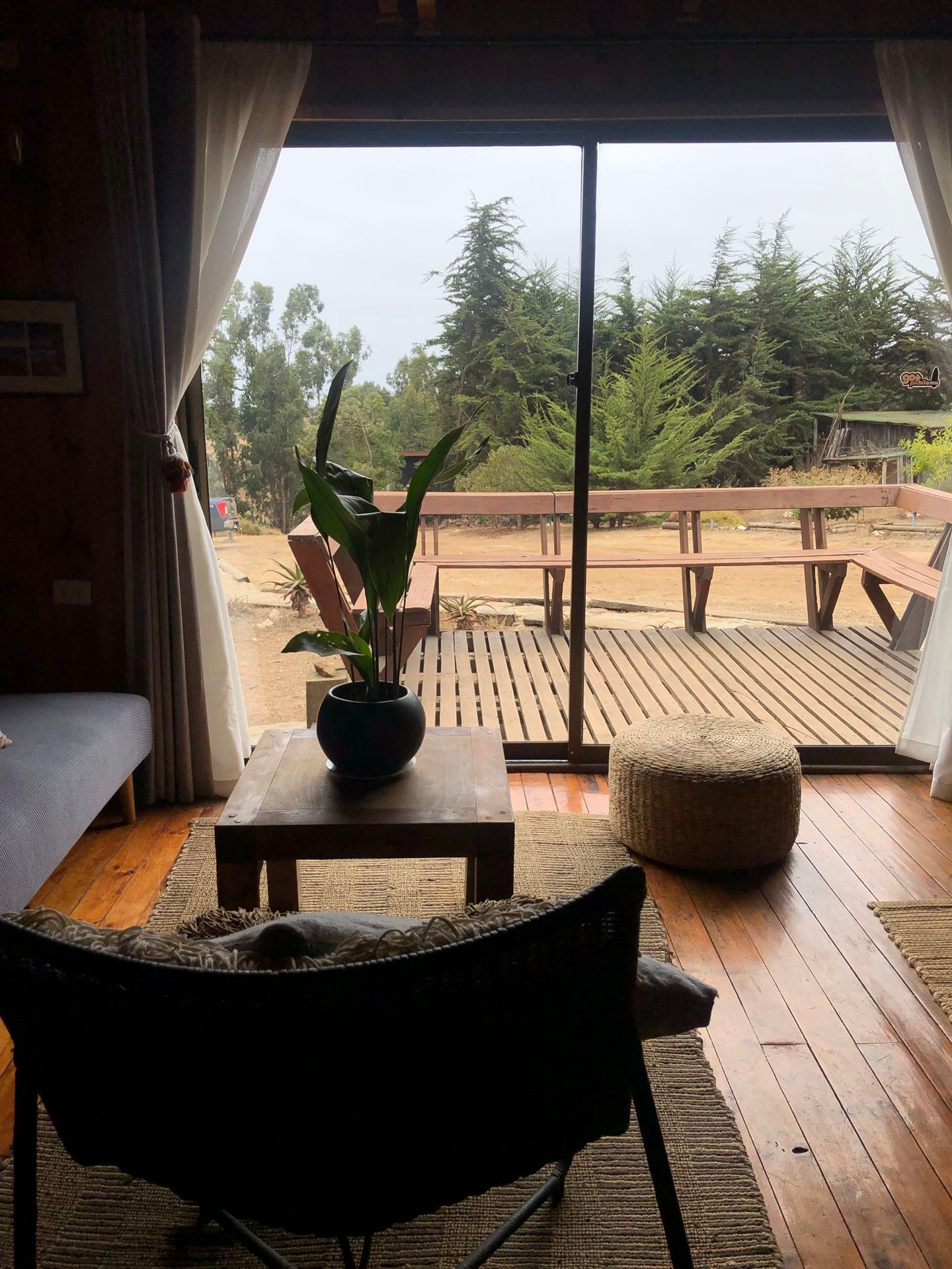 Acogedor interior de cabaña con pisos de madera, ventana grande con vista a una terraza de madera y árboles

