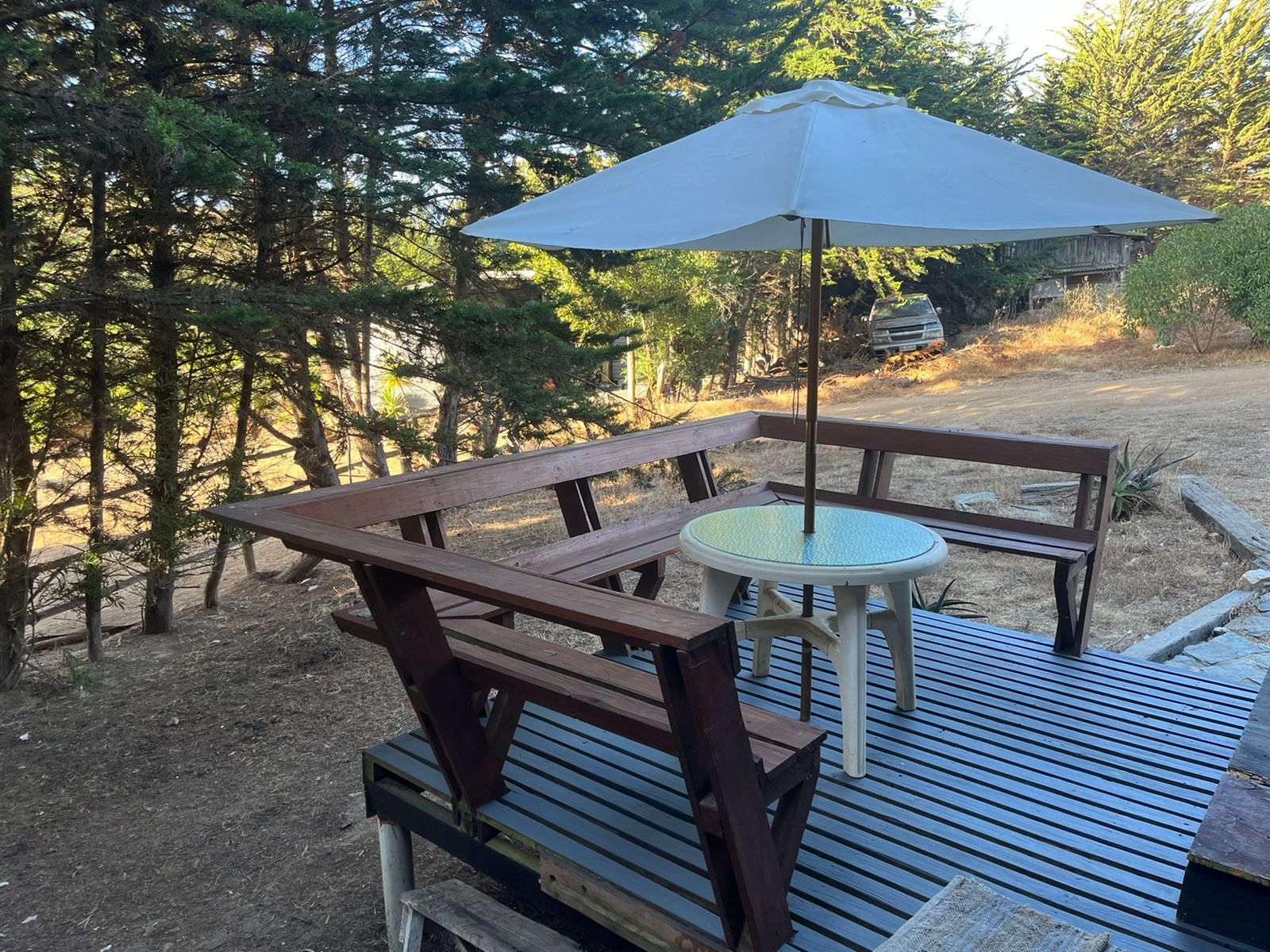 Mesa de picnic con sombrilla en una terraza de madera en una zona boscosa.