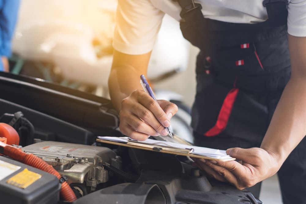 A Mechanic is Writing on a Clipboard While Looking Under the Hood of a Car — Genesis Automotive Services In Lavington, NSW