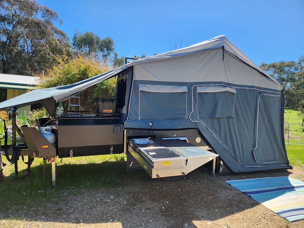 A Camper Trailer with A Tent Attached to It Is Parked in A Grassy Area — Genesis Automotive Services in Lavington, NSW