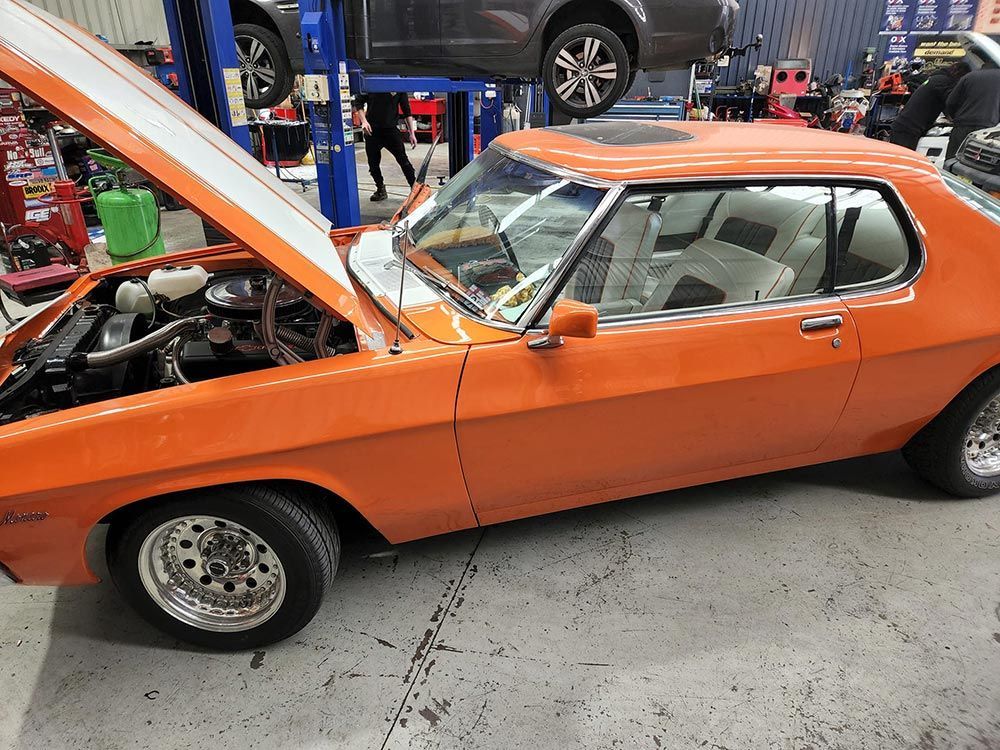 An Orange Car with The Hood up In a Garage  — Genesis Automotive Services in Lavington, NSW