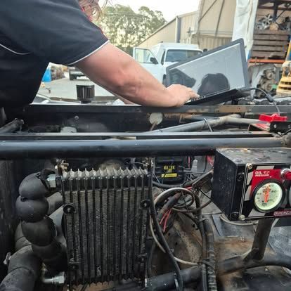 Mechanic working on an engine, using a laptop. Outdoor setting, machinery visible, with gauges.— Genesis Automotive Services in Lavington, NSW