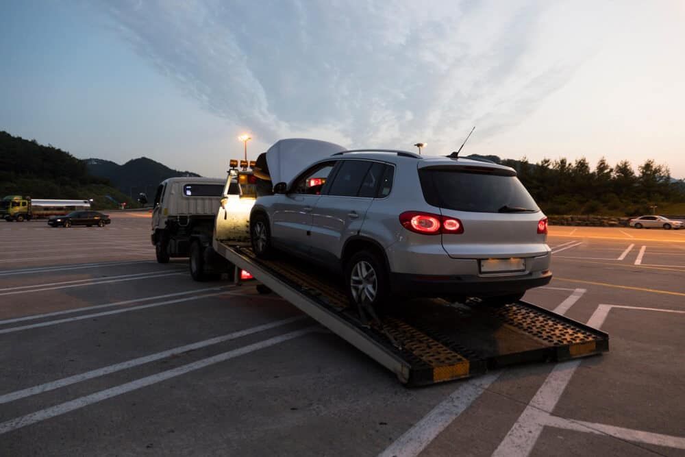 A Car is Being Towed by a Tow Truck in a Parking Lot — Genesis Automotive Services In Lavington, NSW