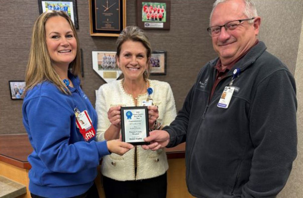 Three people holding a plaque indoors. Two women and a man, smiling.
