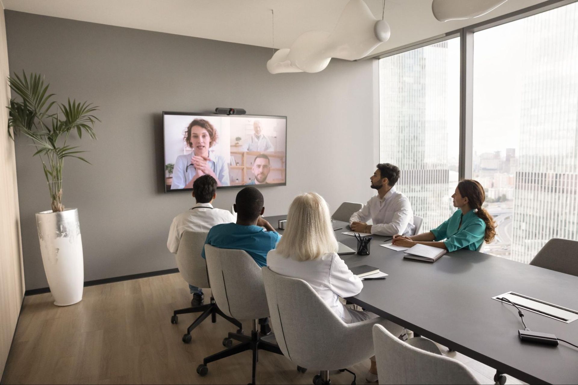 a group of people at a conference table meeting virtually with others on a TV