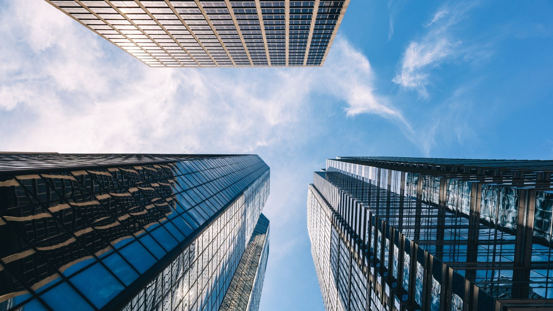 Looking up between modern glass skyscrapers against a blue sky with clouds