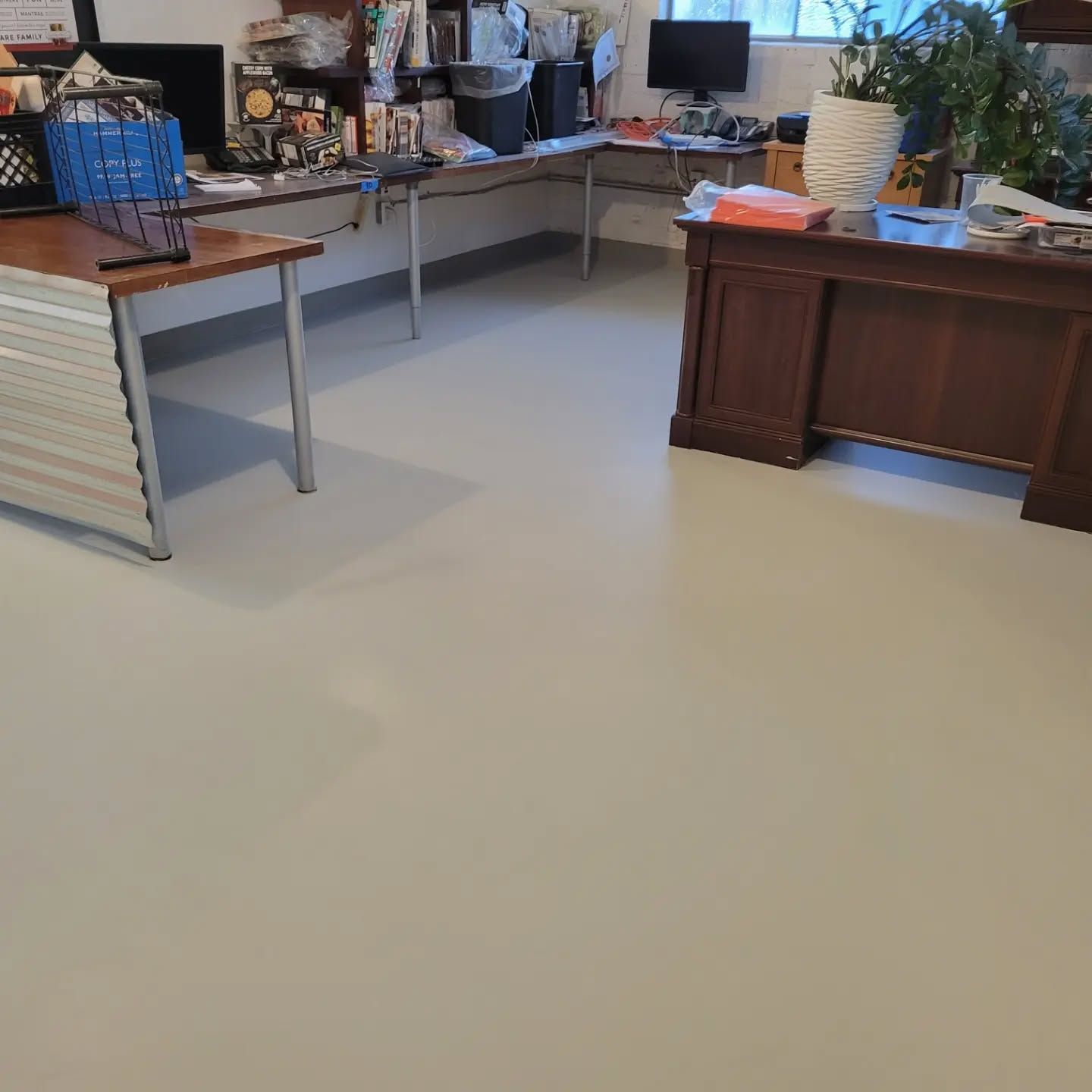 Basement office with light gray floor, tables, desk, and items on shelves.
