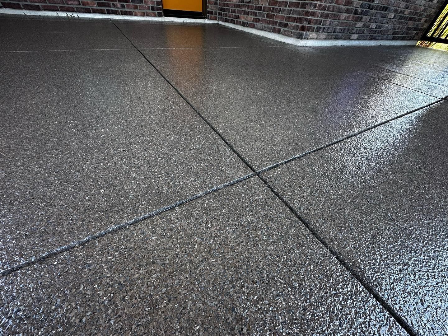 Textured, wet concrete surface with intersecting dark lines. A brick wall and yellow door are visible in the background.