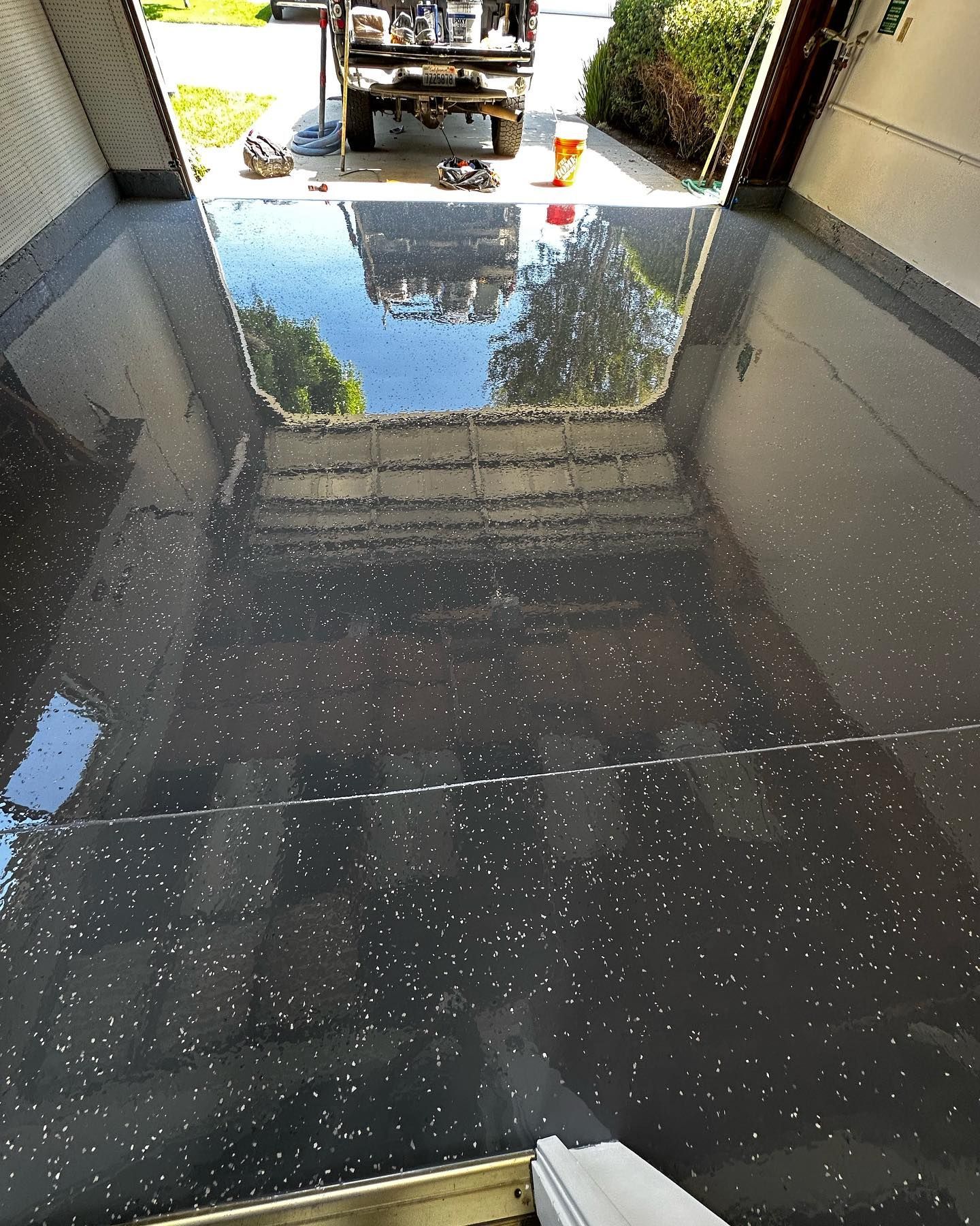 Dark gray epoxy garage floor with reflective flecks. Garage door open to reveal a truck and trees.
