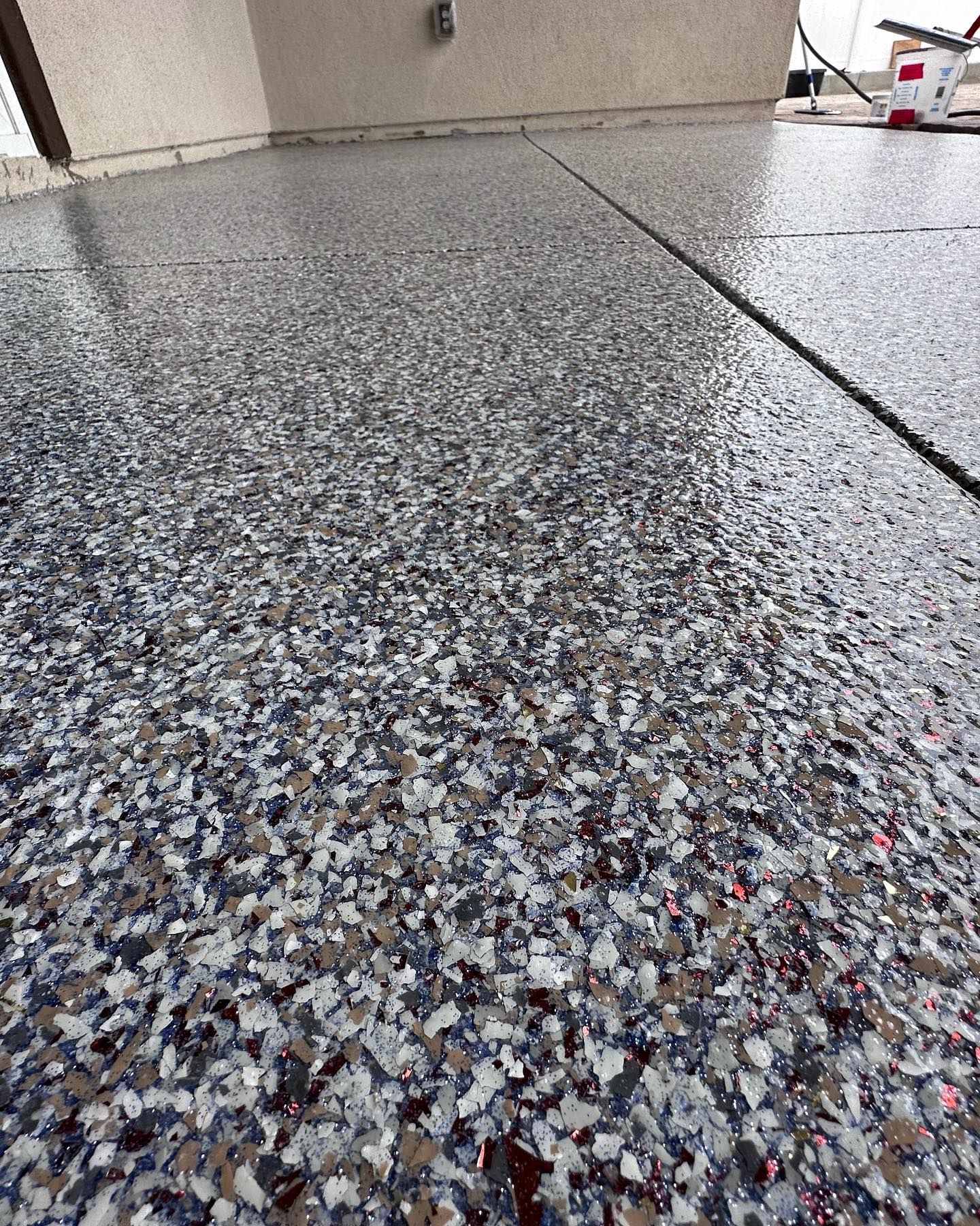 Close-up of a speckled, gray epoxy floor on a patio. Dark line divides the floor.