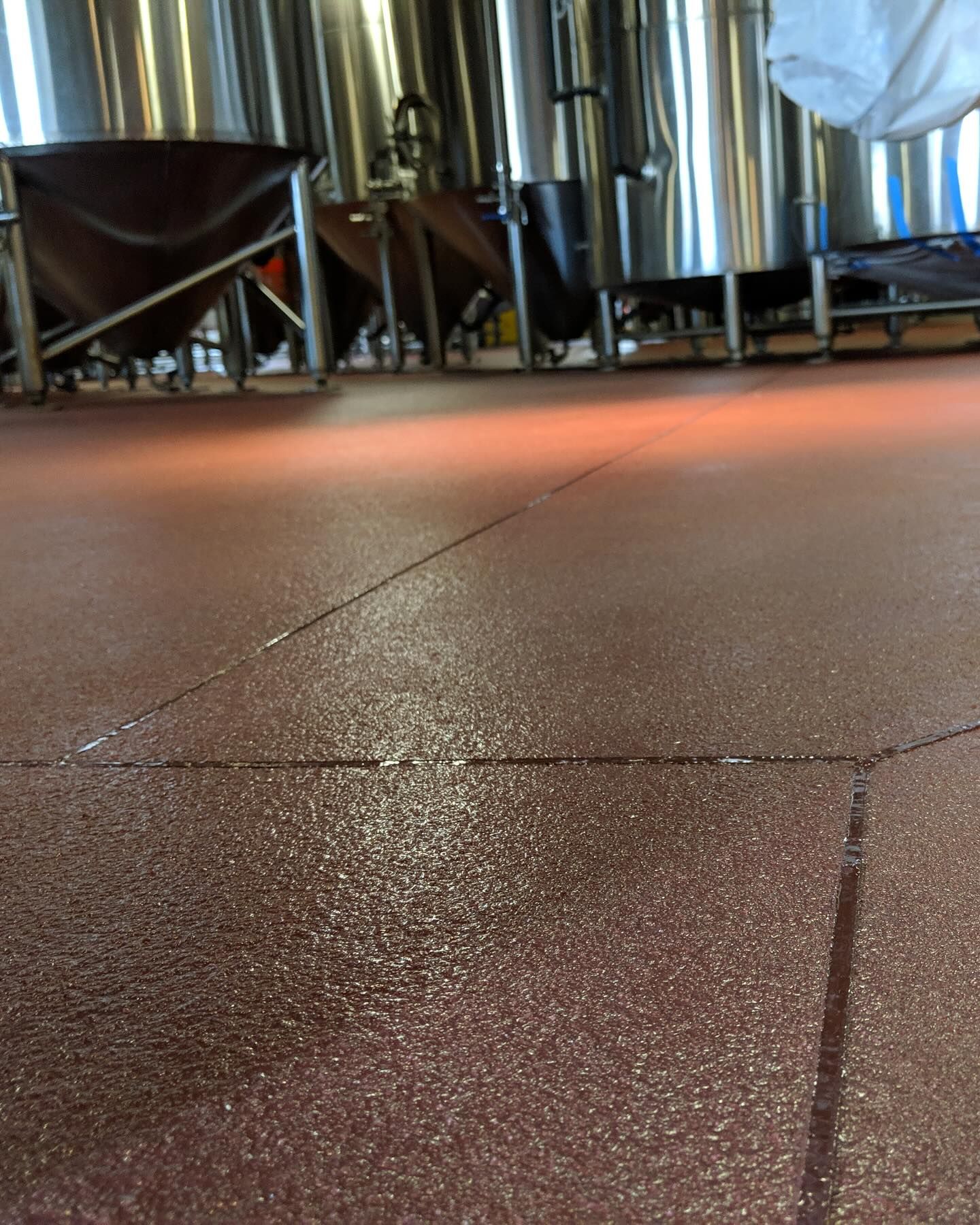 Red speckled floor in a brewery with stainless steel tanks in the background.