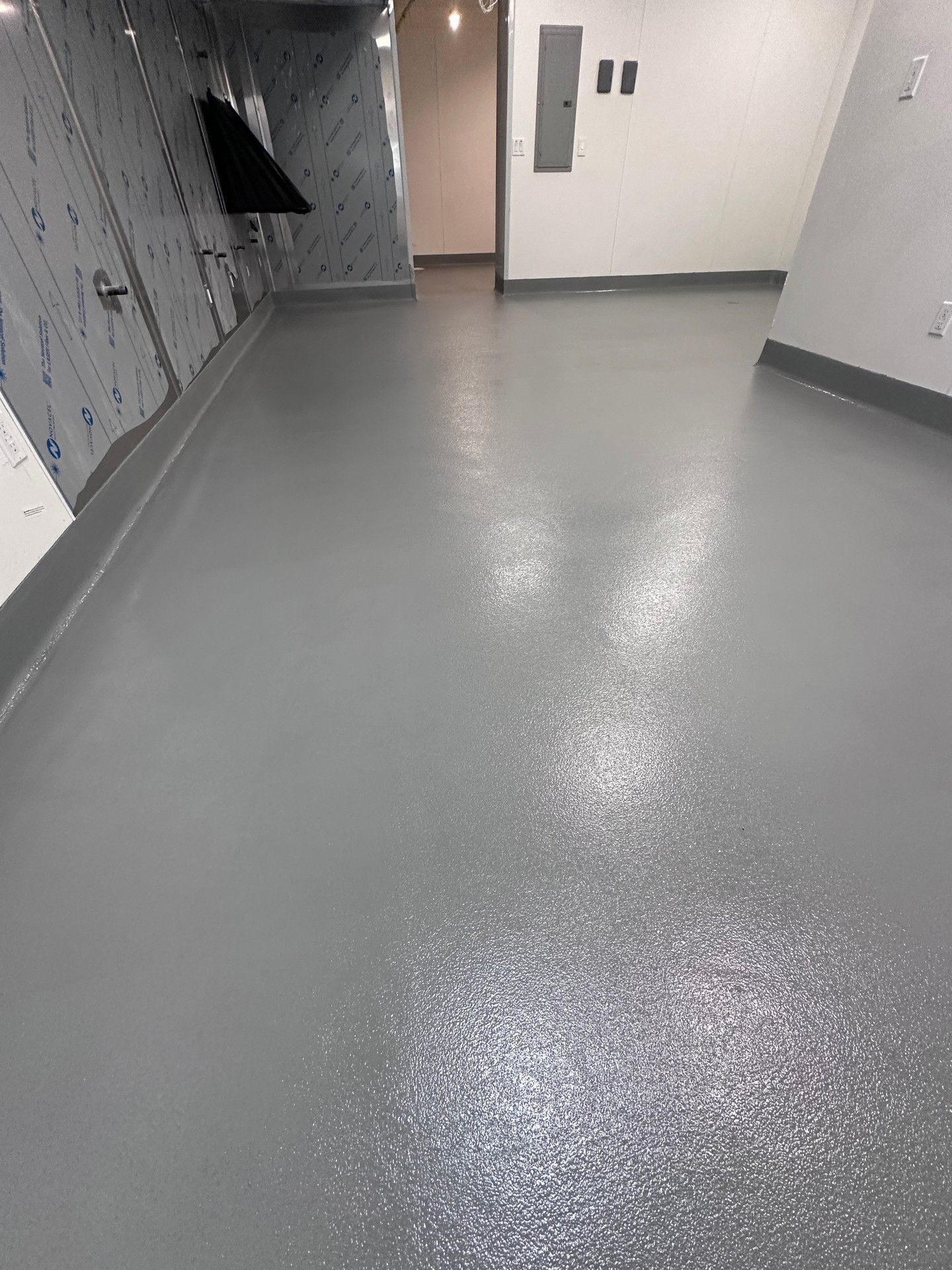 Gray, reflective floor in a hallway with white and silver walls. A door is visible in the distance.