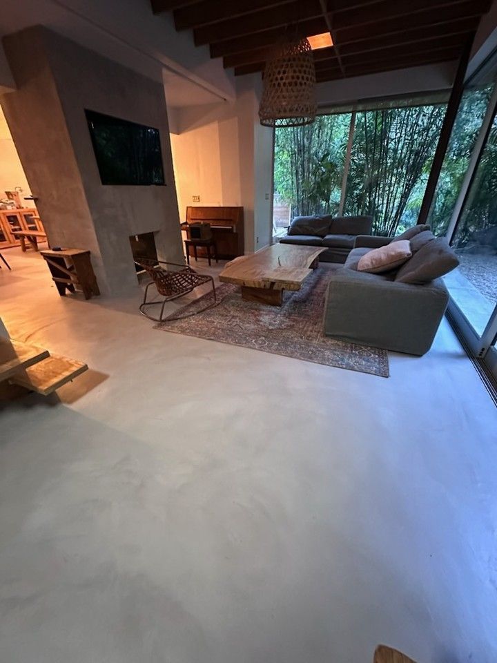 Gray concrete floor in a commercial space, tables with light-colored wood legs, and overhead lighting.