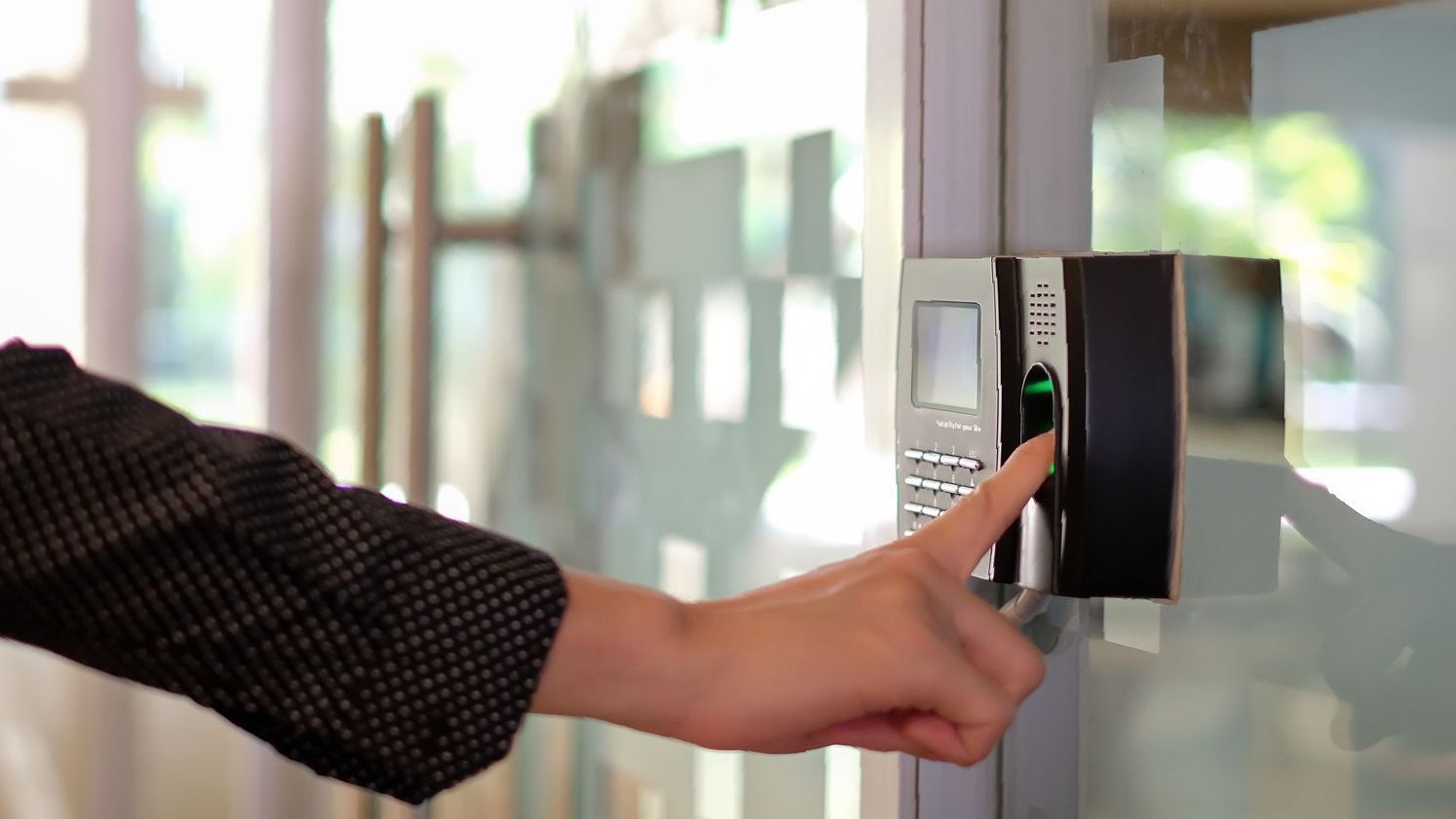 A person using their finger to scan a fingerprint on a security door access control system.