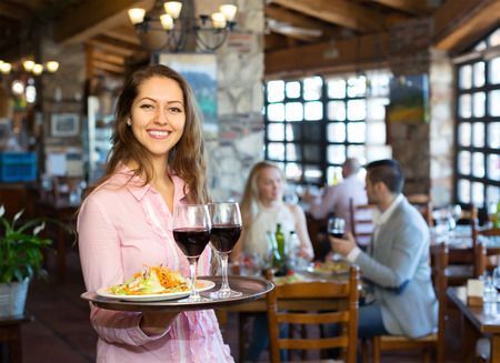 Waitress smiles, carrying tray with food and drinks in restaurant.