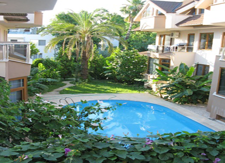 Swimming pool surrounded by lush greenery and buildings.