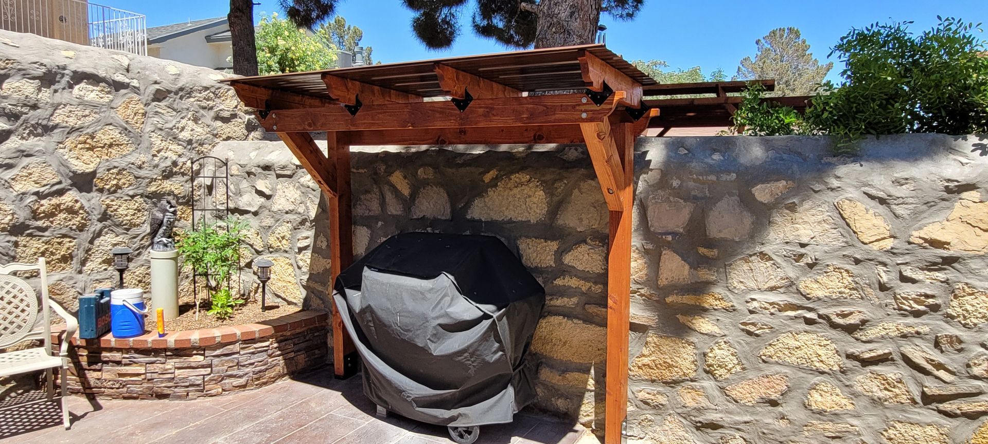 Outdoor grilling area with stone walls, wooden pergola, grill, and patio seating.