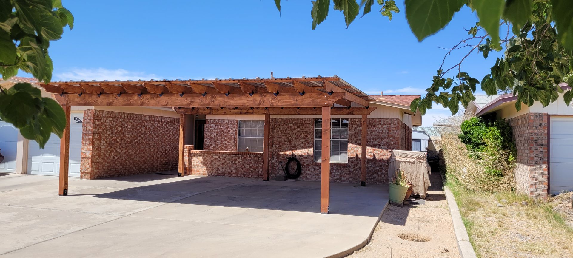 House with a brick facade, a wooden pergola, and a blue sky on a sunny day.