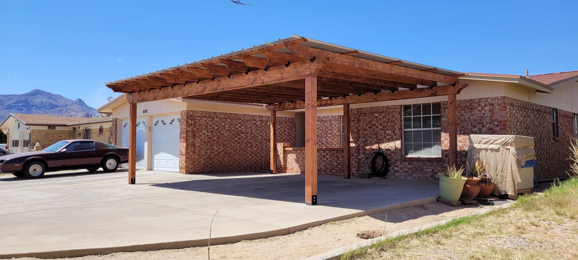 A carport with a wooden pergola attached to a brick house, and a car parked nearby.