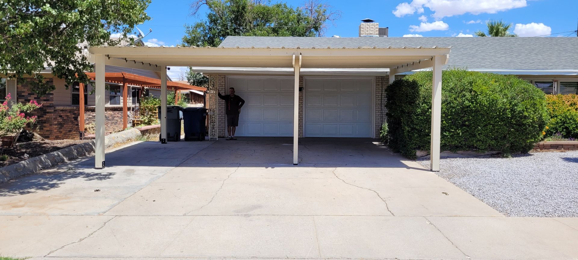 A house with a carport and two garage doors. A person stands in the carport area.