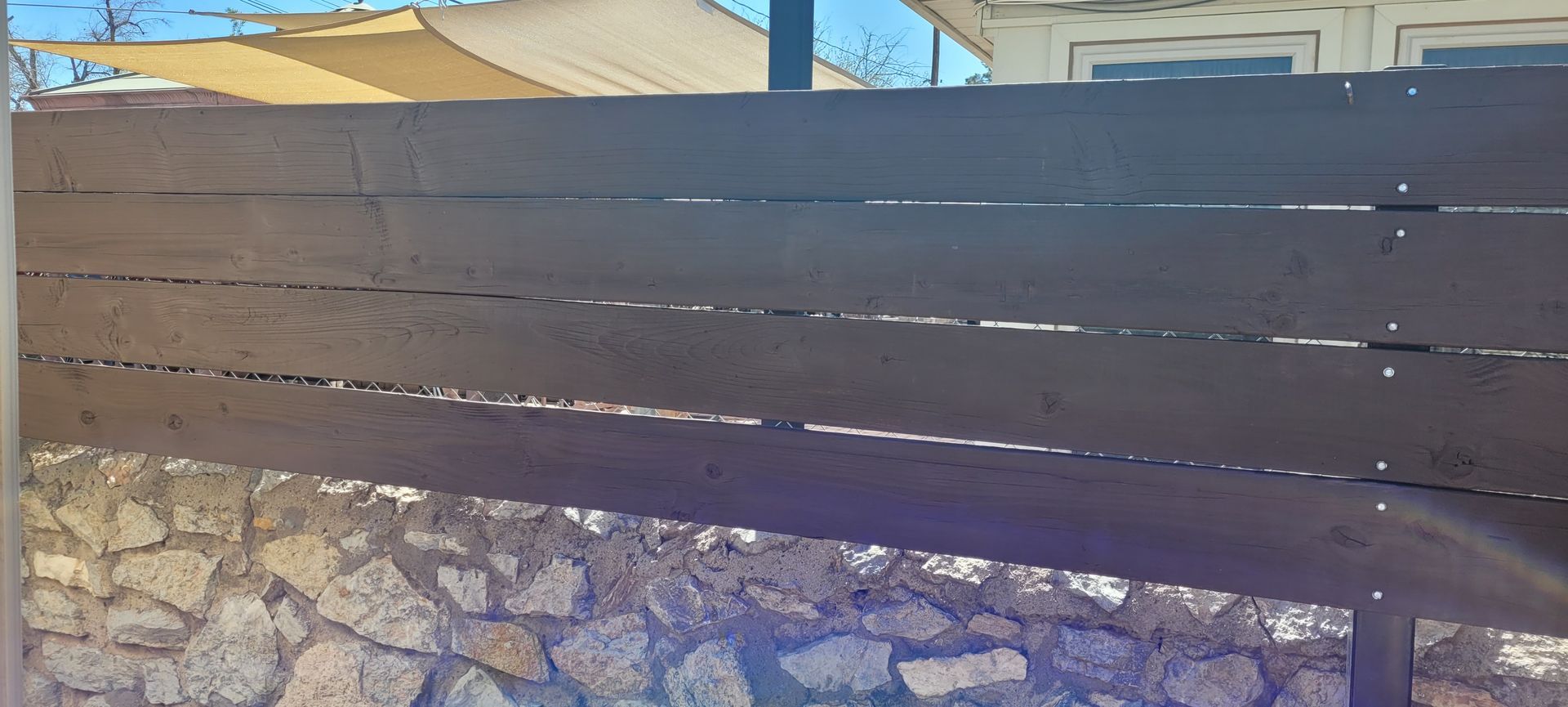 Wooden fence in front of a stone wall. A house and blue sky are in the background.