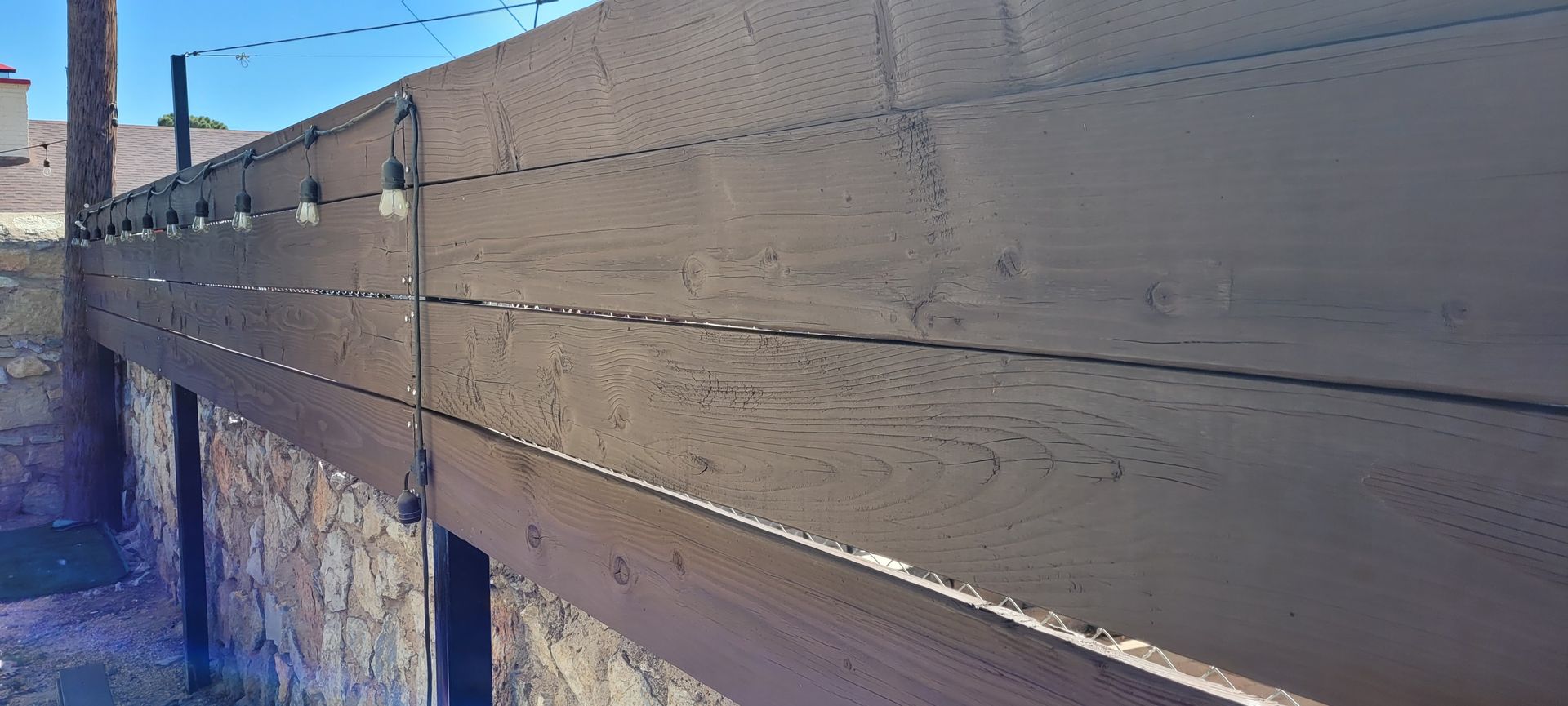 Wooden fence with string lights against a blue sky.