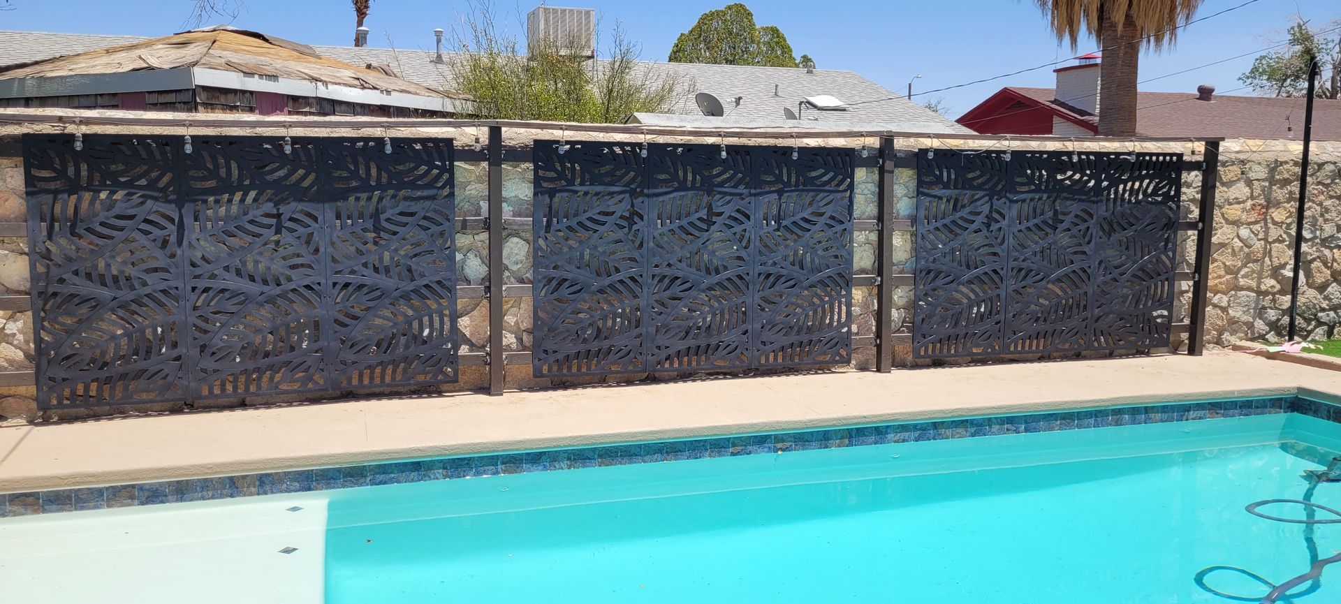Poolside view with a decorative patterned fence. Clear blue sky.