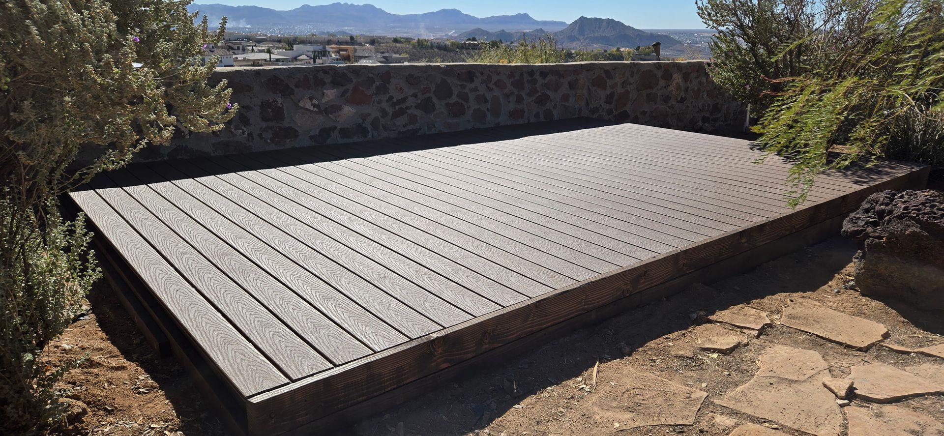 Wooden deck with a patterned design outdoors, with a view of distant mountains.