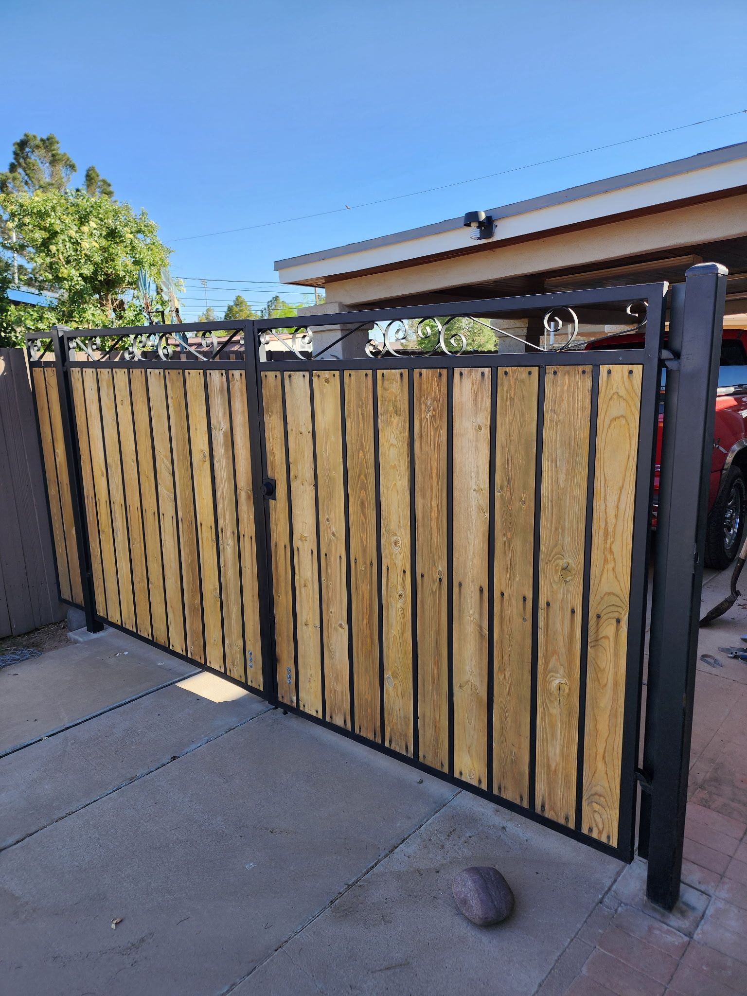 Wooden and metal gate in driveway; vertical wood planks, black metal frame.