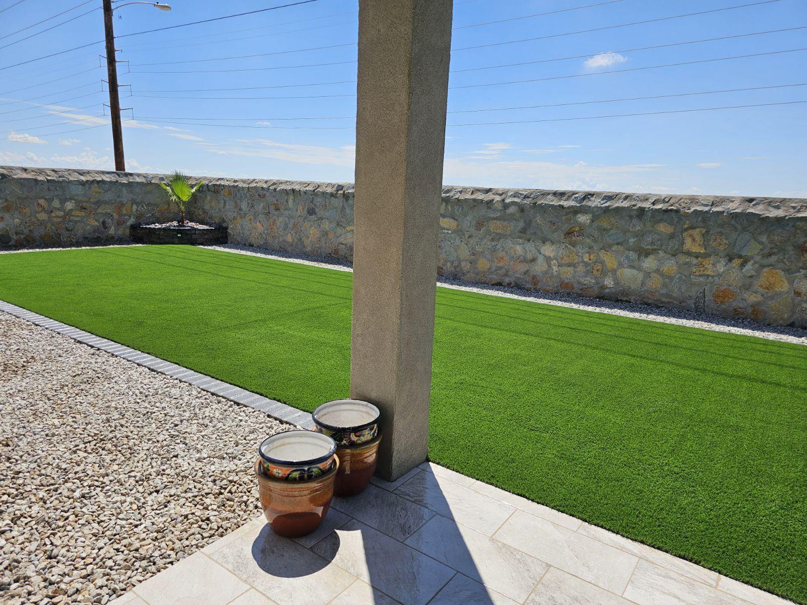 A patio with artificial green grass and a stone wall on a sunny day.