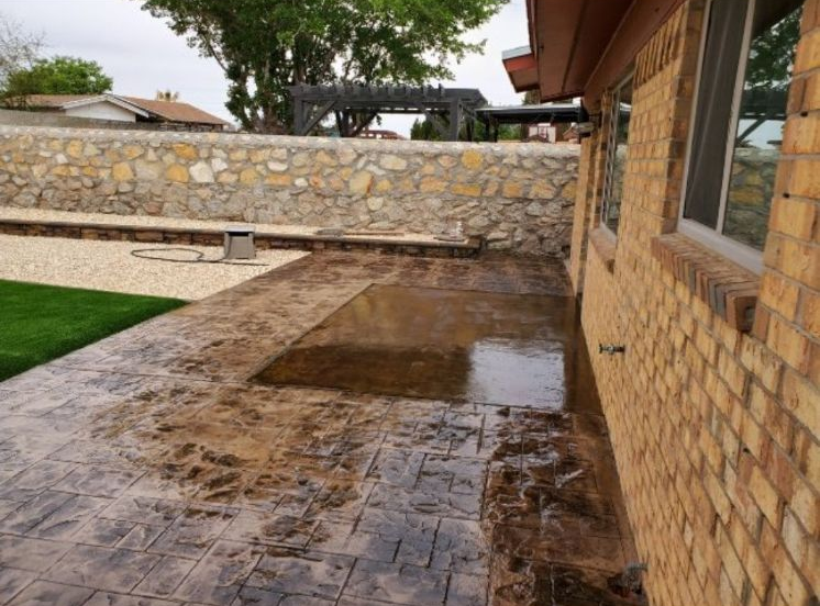 Brick house with a stamped concrete patio; the patio is wet with a stone retaining wall in the background.